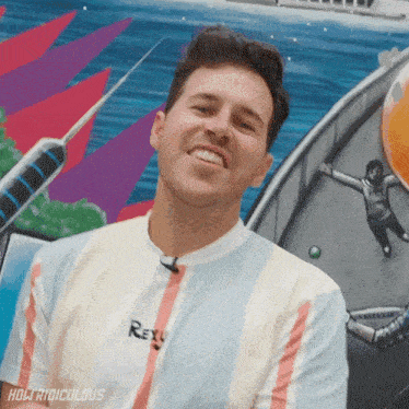 a man in a rexy shirt smiles in front of a painting