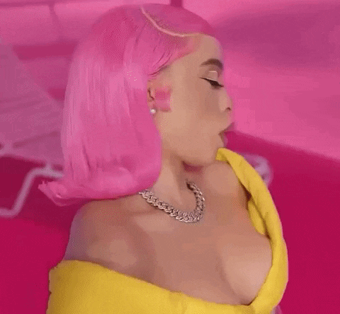 a woman with pink hair and a yellow dress is standing in front of a pink wall .
