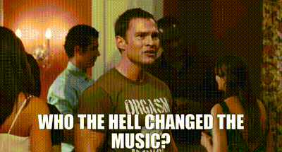 a man wearing a shirt that says " orgasm " stands in a crowd of people .