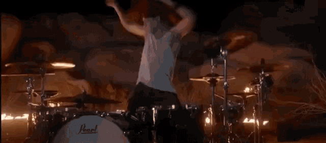 a man is playing drums in front of a rock wall with fire in the background .