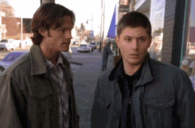 two men standing next to each other on a sidewalk in front of a building