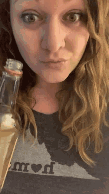 a woman wearing a shirt that says proud is holding a bottle of alcohol .