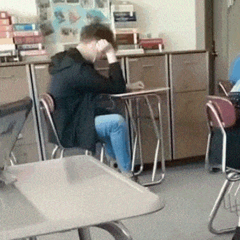 a man is sitting at a desk in a classroom with his hands on his head