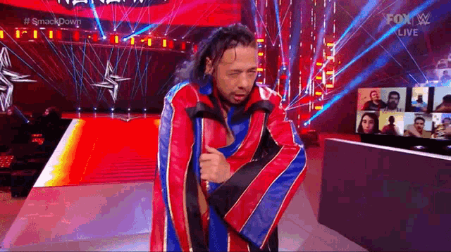 a man in a colorful jacket is walking down a red carpet on a stage .