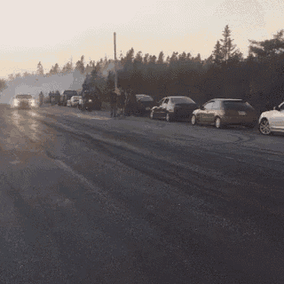 a group of people are standing on the side of a road watching a car drift