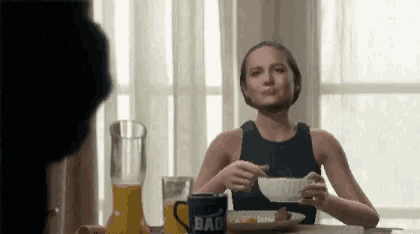 a woman is sitting at a table with a mug that says bad on it