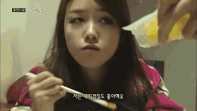 a woman in a pink shirt is eating with chopsticks while a person pours sauce on her face