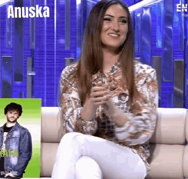 a woman is sitting on a couch in front of a sign that says anuska