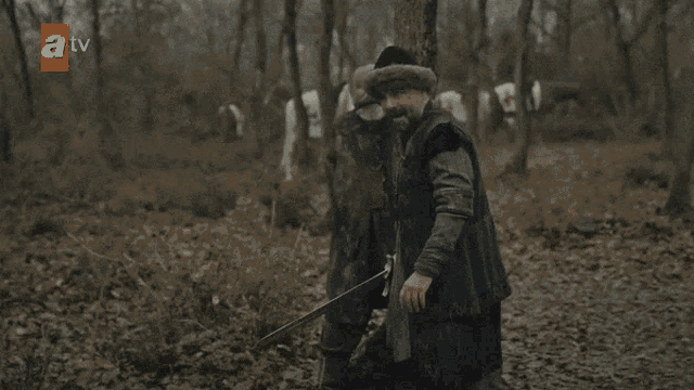 a group of men are fighting in a forest with a tv logo in the corner