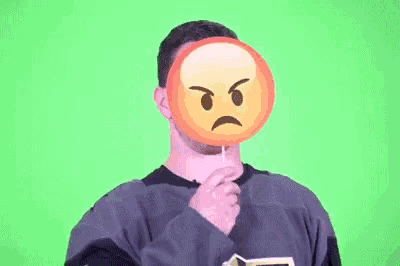a man is holding a lollipop in front of his face with an angry face on it .