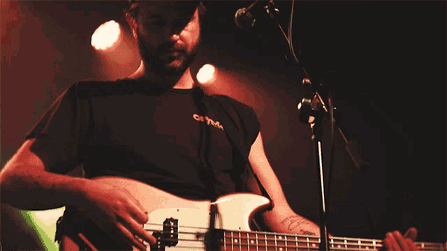 a man playing a bass guitar with a black shirt that says ' oasis ' on the front