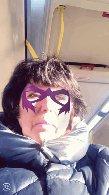 a woman with a purple mask on her face is sitting on a bus