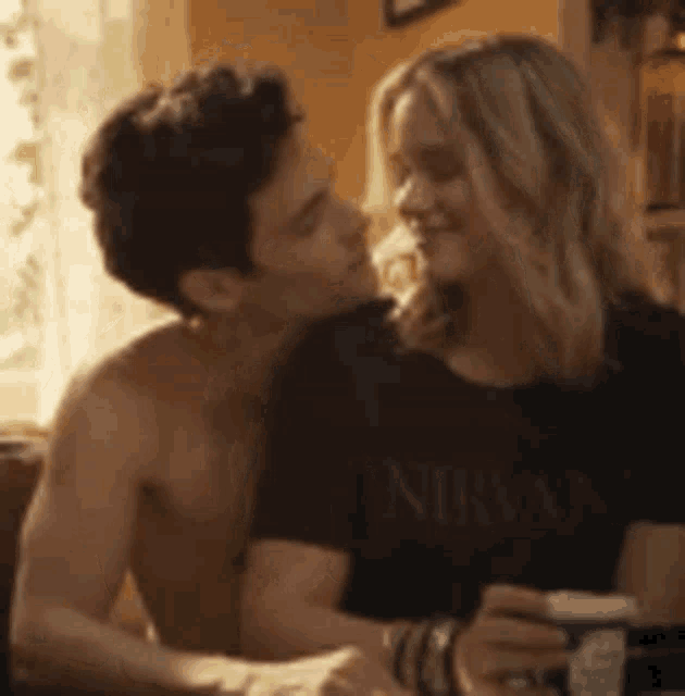 a man and a woman are kissing in a living room . the woman is wearing a nirvana shirt .