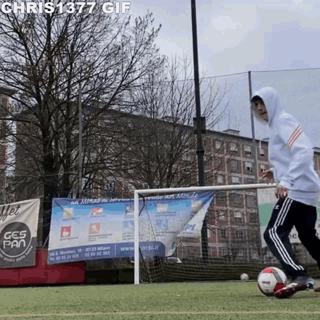 a man in a hoodie is kicking a soccer ball on a field