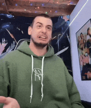 a man in a green hoodie is making a funny face while sitting in a room .