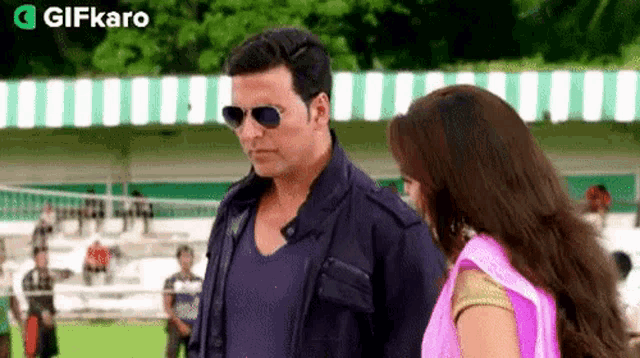 a man wearing sunglasses is standing next to a woman in a pink sari .