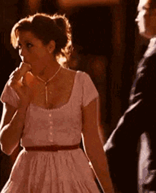 a woman in a pink dress is eating ice cream while standing next to a man in a suit .