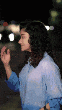 a woman with curly hair wearing a blue shirt is waving her hand
