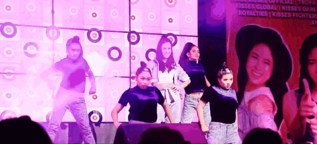 a group of girls are dancing on a stage in front of a sign that says kisses global