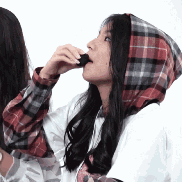 a girl wearing a plaid hoodie is eating a chocolate bar
