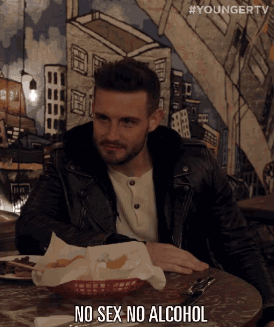 a man in a leather jacket sits at a table with a basket of chips and says no sex no alcohol