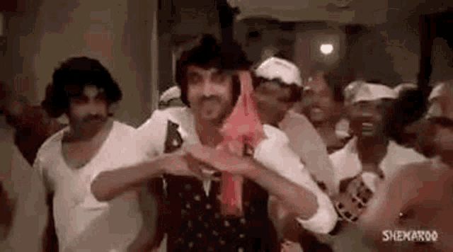 a group of men are dancing together in a room while a man is holding a red towel around his neck .