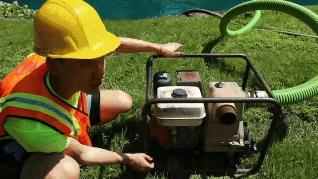 a man wearing a yellow hard hat and safety vest is working on a pump