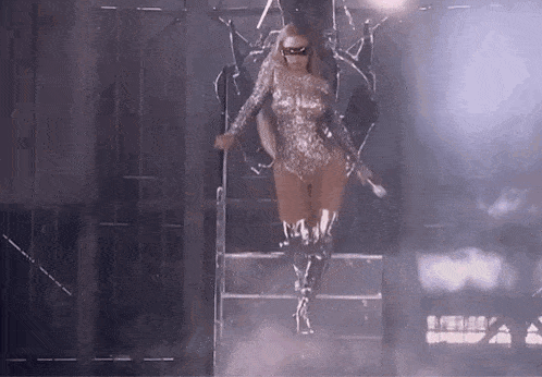 a woman in a silver bodysuit and knee high boots is standing on a stage .