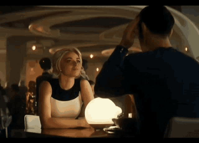 a man and a woman are sitting at a table looking at each other in a restaurant .