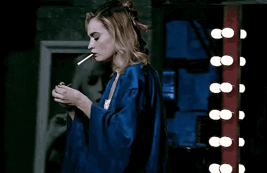 a woman in a blue robe is smoking a cigarette in a room .
