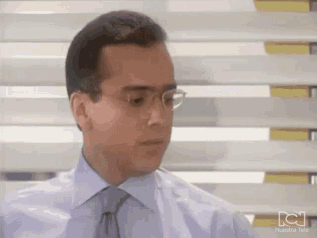 a man wearing glasses and a white shirt with a nuestra tele logo on the bottom