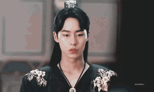 a young man with long hair and a crown on his head is wearing a black dress .