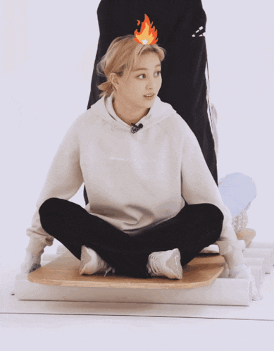 a woman wearing a champion sweatshirt sits on a wooden board