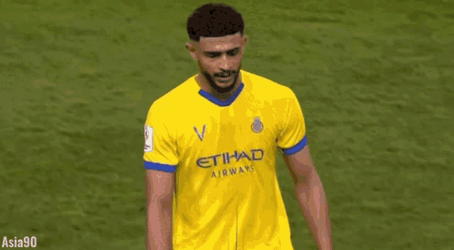 a soccer player wearing a yellow and blue etihad airways jersey is standing on a field .