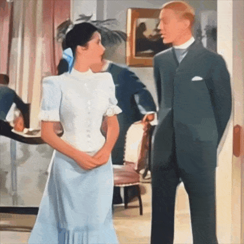 a man in a suit stands next to a woman in a light blue dress