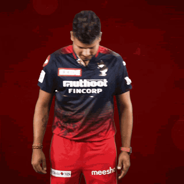 a man wearing a shirt that says exide muthoot fincorp stands in front of a red background