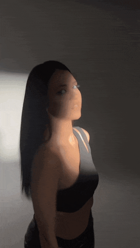 a woman in a black one shoulder top is standing in a dark room