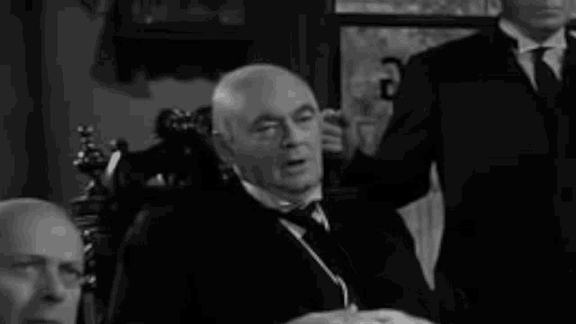 a man in a suit and tie is sitting in a chair in a room with other men .