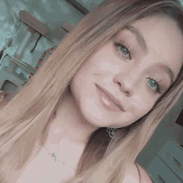 a woman with long blonde hair and green eyes is smiling