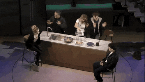 a group of people are sitting around a kitchen counter with a bowl of food on it