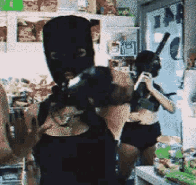a man wearing a ski mask is holding a gun in a kitchen .