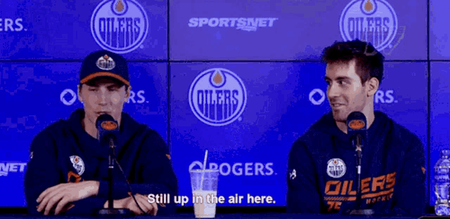 two men are sitting in front of a screen that says oilers on it