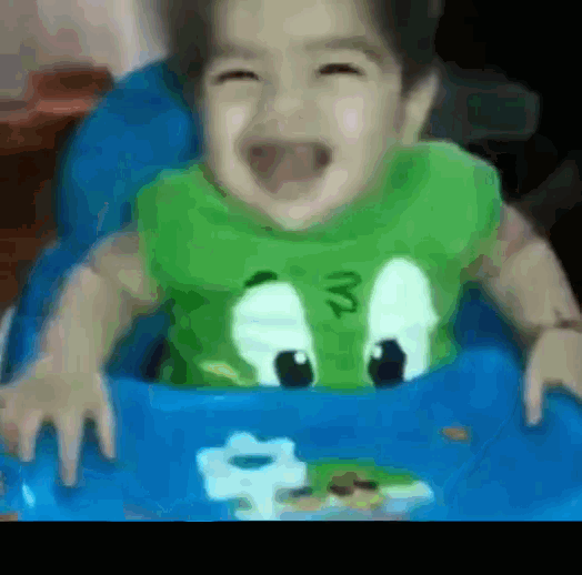 a baby wearing a green frog shirt is sitting in a high chair and smiling
