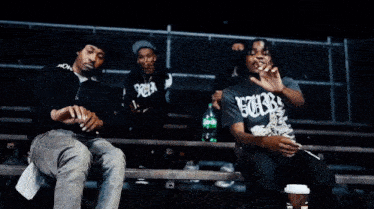 three men are sitting on a bench with one wearing a shirt that says " smoke "