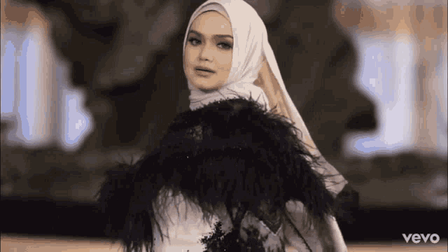 a woman wearing a white hijab and a black cape with the word vevo on the bottom right