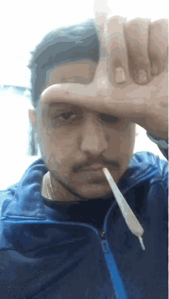a man in a blue jacket is holding a thermometer in his mouth