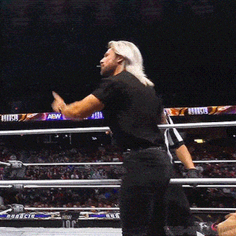 a wrestler in a black shirt is standing in a wrestling ring with a referee .