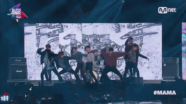a group of young men are performing on a stage with a large screen behind them that says mnet