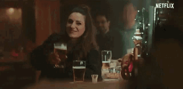 a woman is sitting at a bar holding a glass of beer and a shot glass .