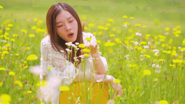 a woman in a white dress is blowing flowers in a field of yellow flowers .